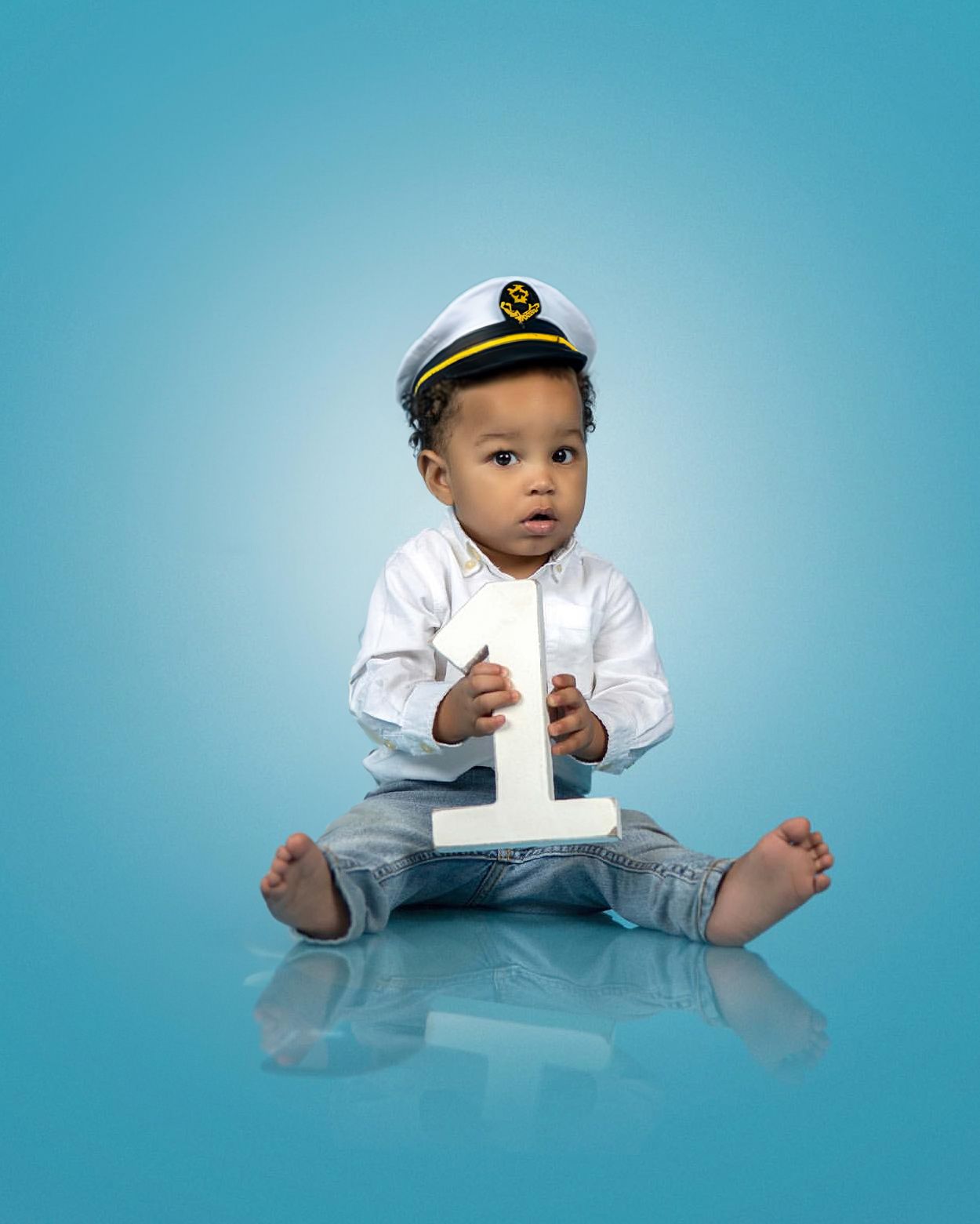 Nautical themed first birthday portrait with sailor cap against blue background.