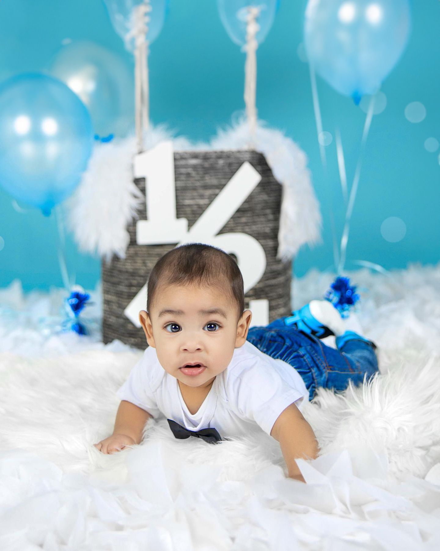 6-month milestone photo on white fur with blue balloon decorations.
