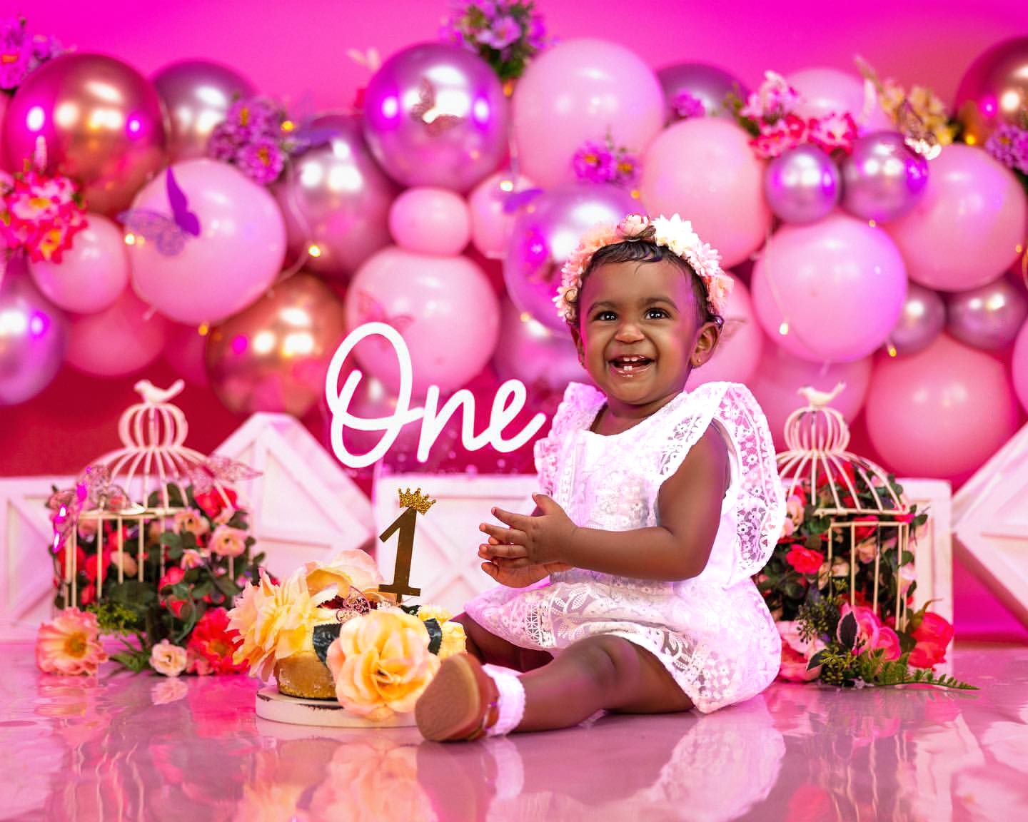 Pink balloon backdrop with decorative birdcages for first birthday photoshoot.