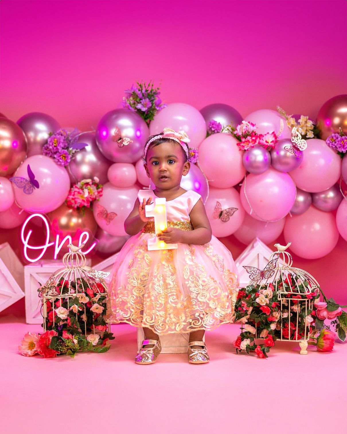 Pink and gold first birthday setup with decorative birdcages and balloon wall.