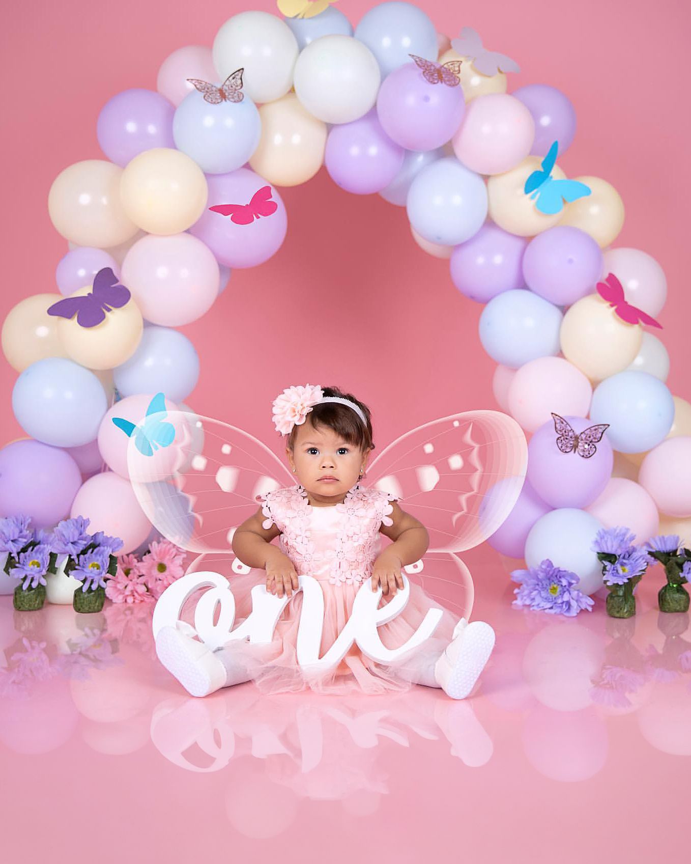 Butterfly themed first birthday with pastel balloon arch and wings.