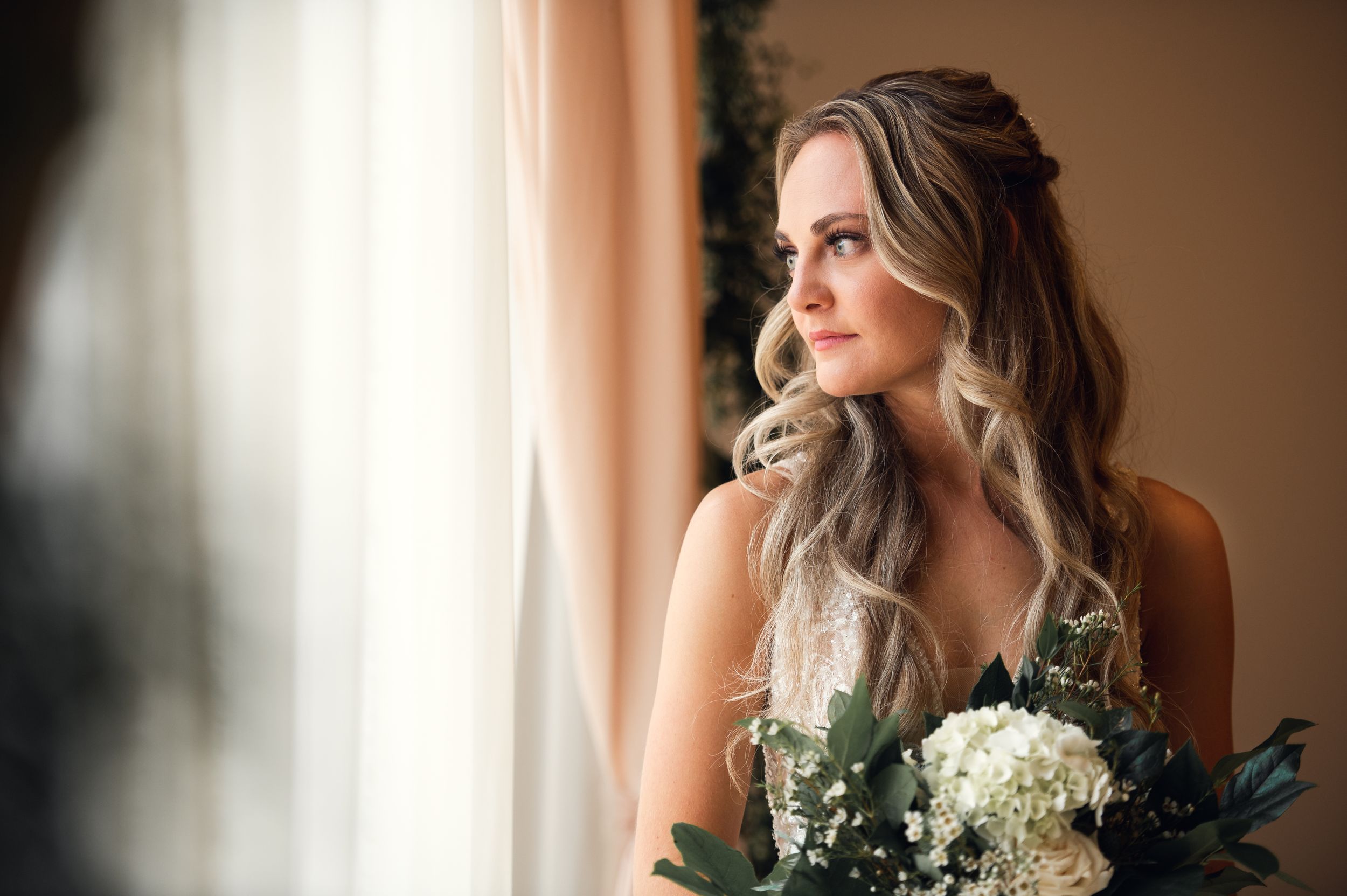 Elegant bridal portrait by window with soft natural light and white floral bouquet.