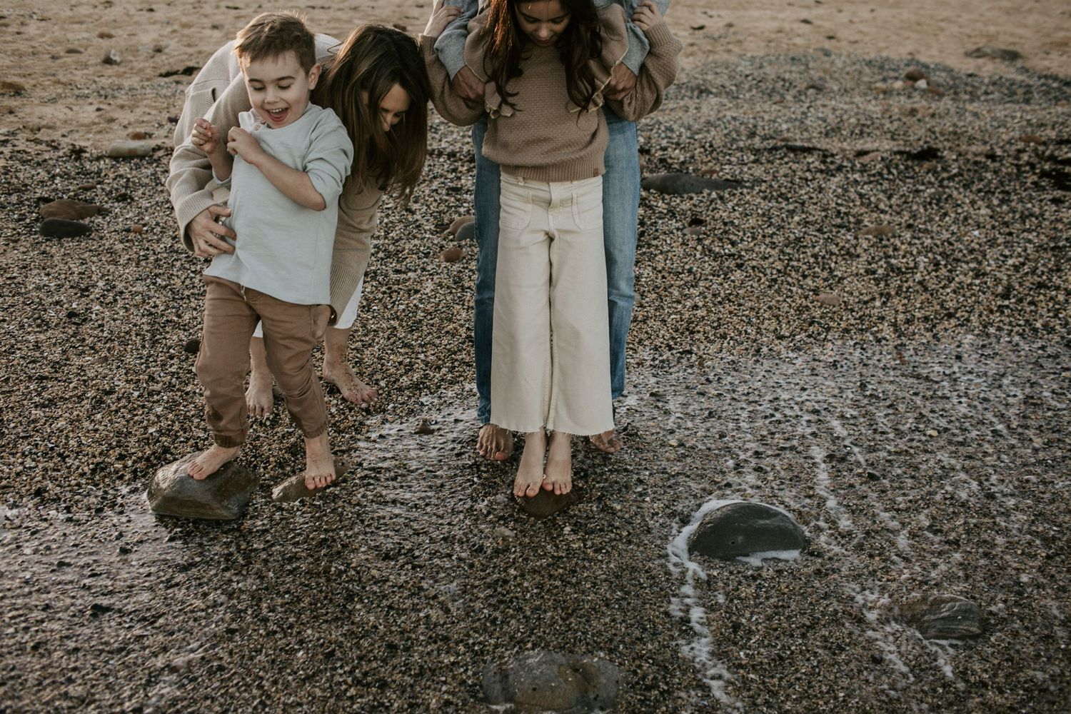 Mother and two children explore rocky beach tide pools together in casual outdoor family session.