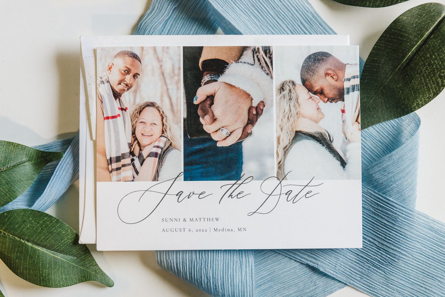 Save the date card with engagement photos laid on white surface with green leaves.