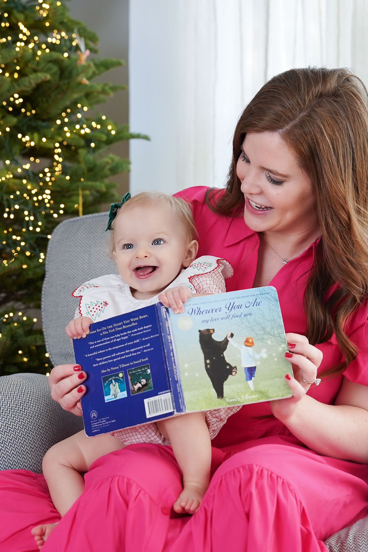 an ifaqnt sits on her mothers lap reading a book with a Christmas tree behind them during an in home photography session