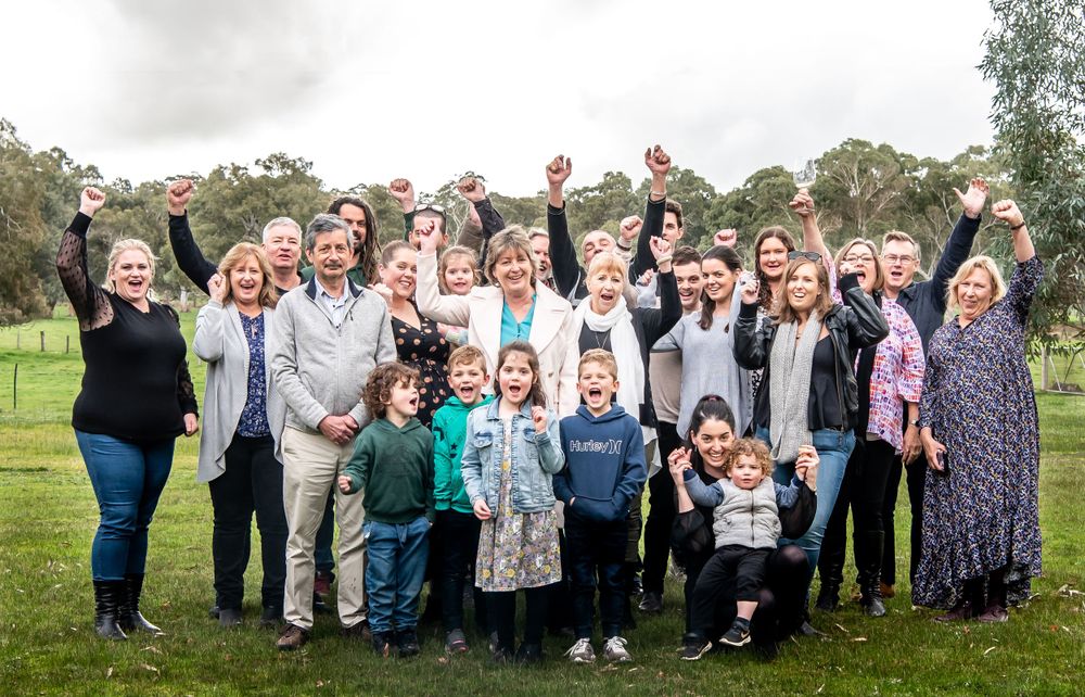 A large group of people gathered outdoors raising their arms in celebration at a countryside event.