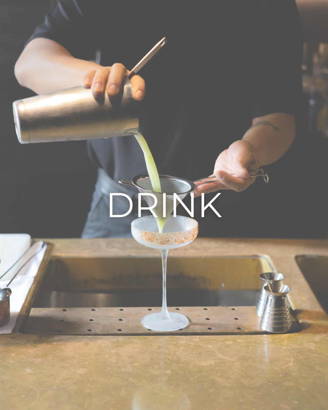 Bartender pouring a craft cocktail from a shaker into a martini glass with text overlay reading 'DRINK'.