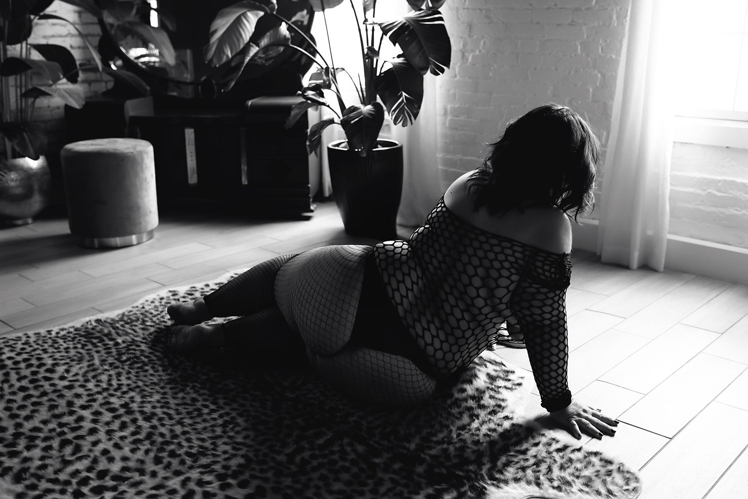 Artistic black and white boudoir photo on leopard print rug with natural window light.