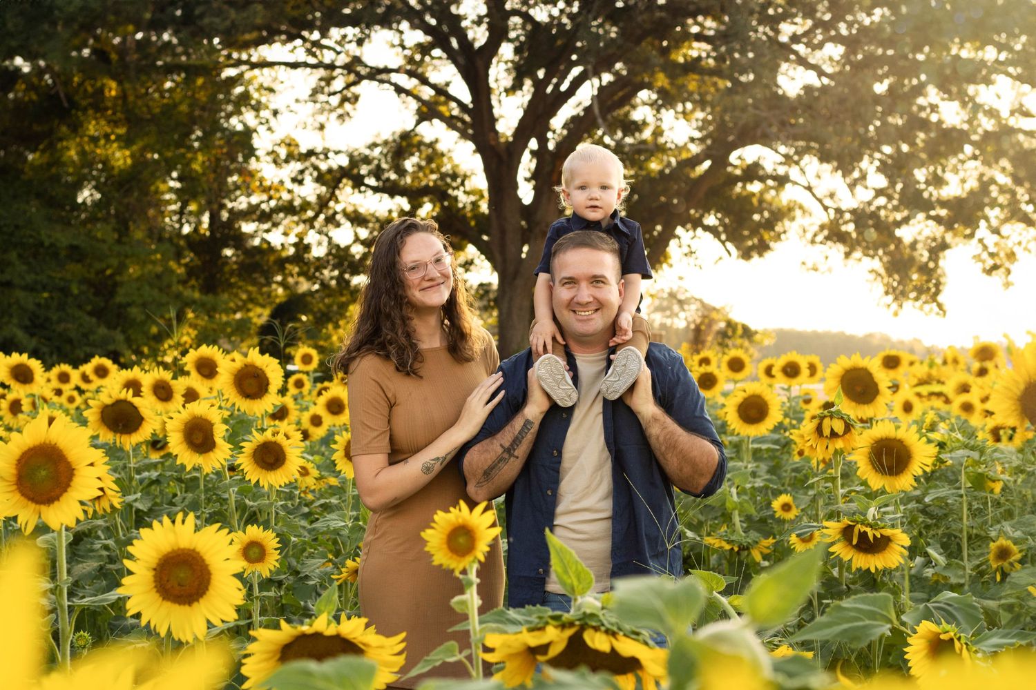 Family with young child poses in field of blooming sunflowers