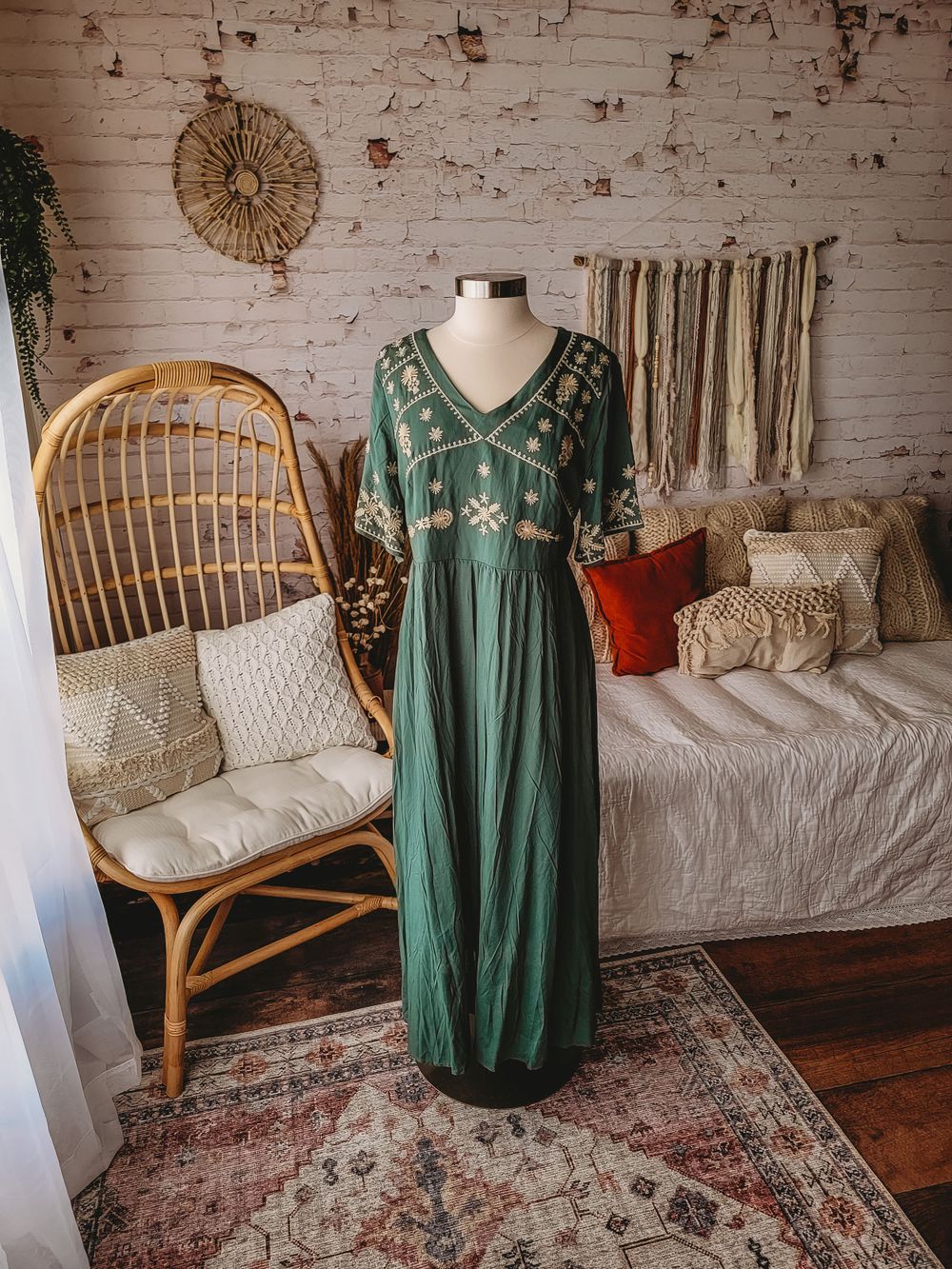 Forest green embroidered V-neck maxi dress with floral details on mannequin in rustic boho room.