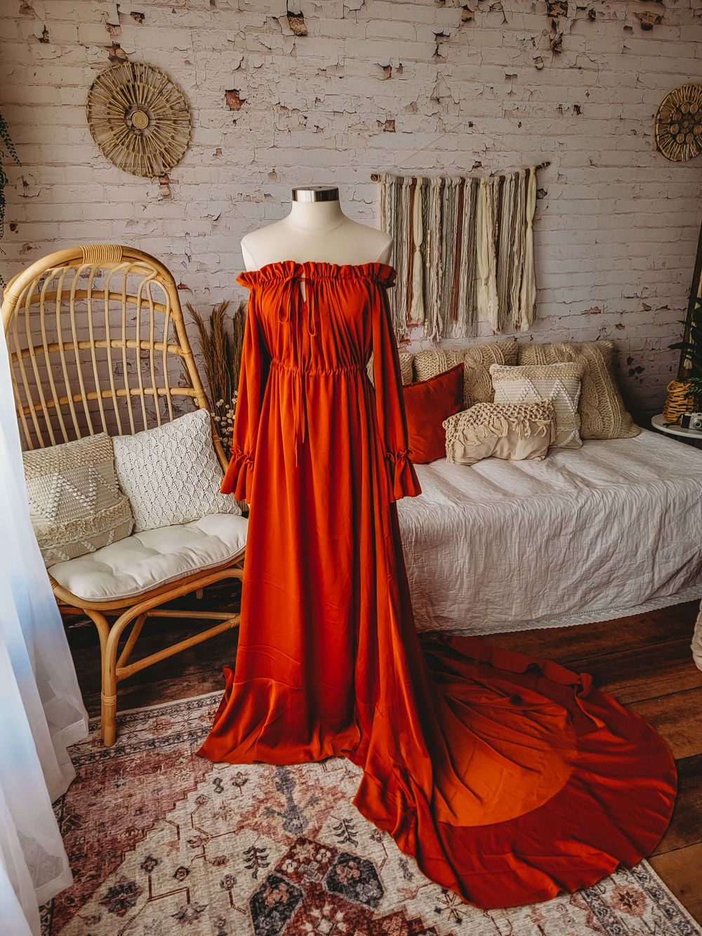 Rust orange off-shoulder maxi dress with dramatic train and bell sleeves on mannequin in boho studio.