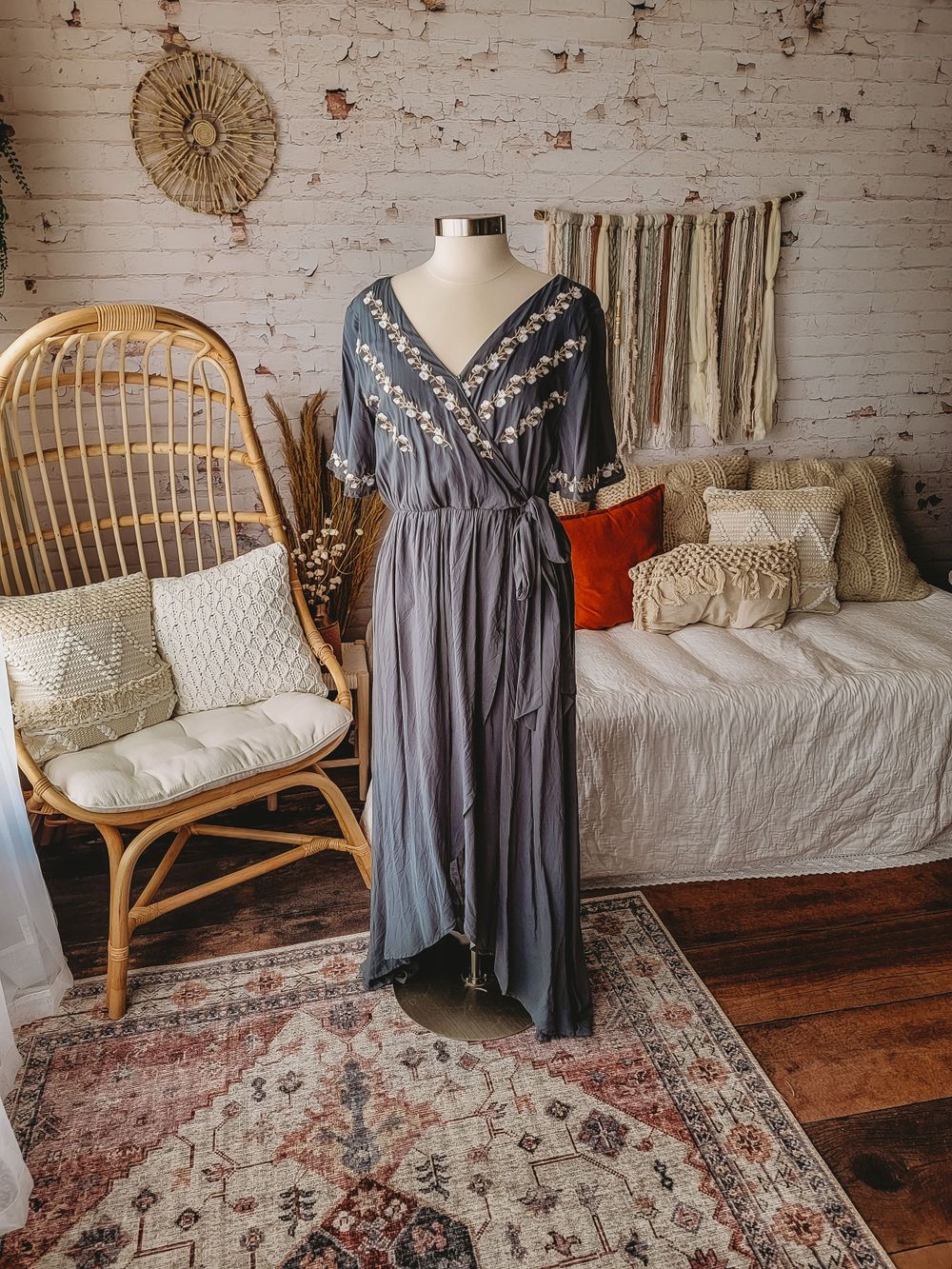Slate blue embroidered wrap maxi dress with floral details and tie waist on mannequin.