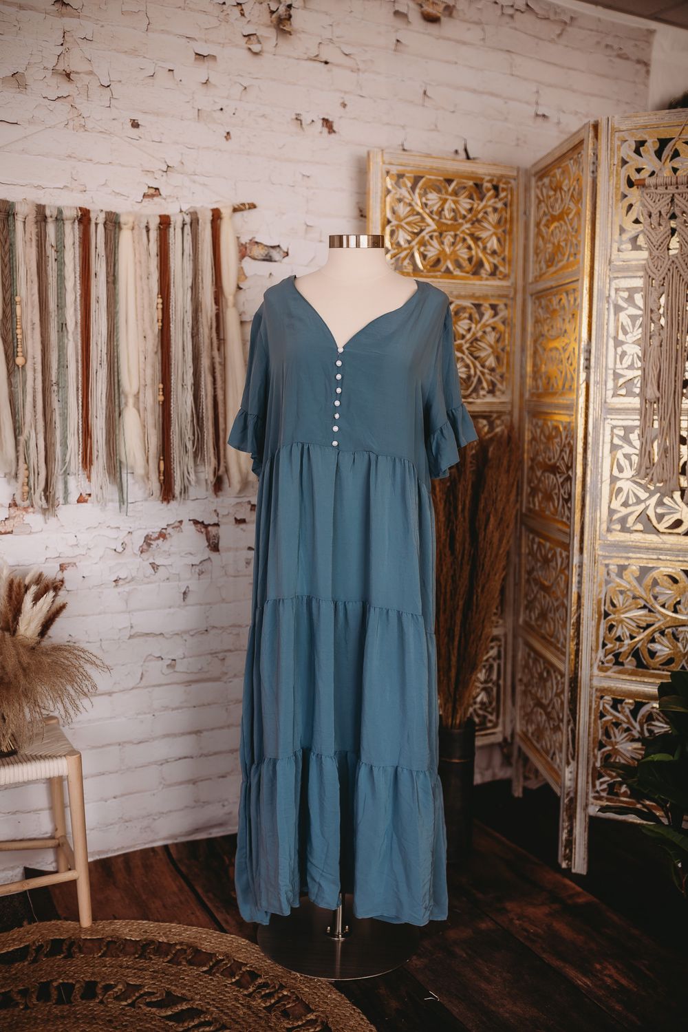Teal blue button-front short sleeve tiered maxi dress on mannequin in boho boutique setting.