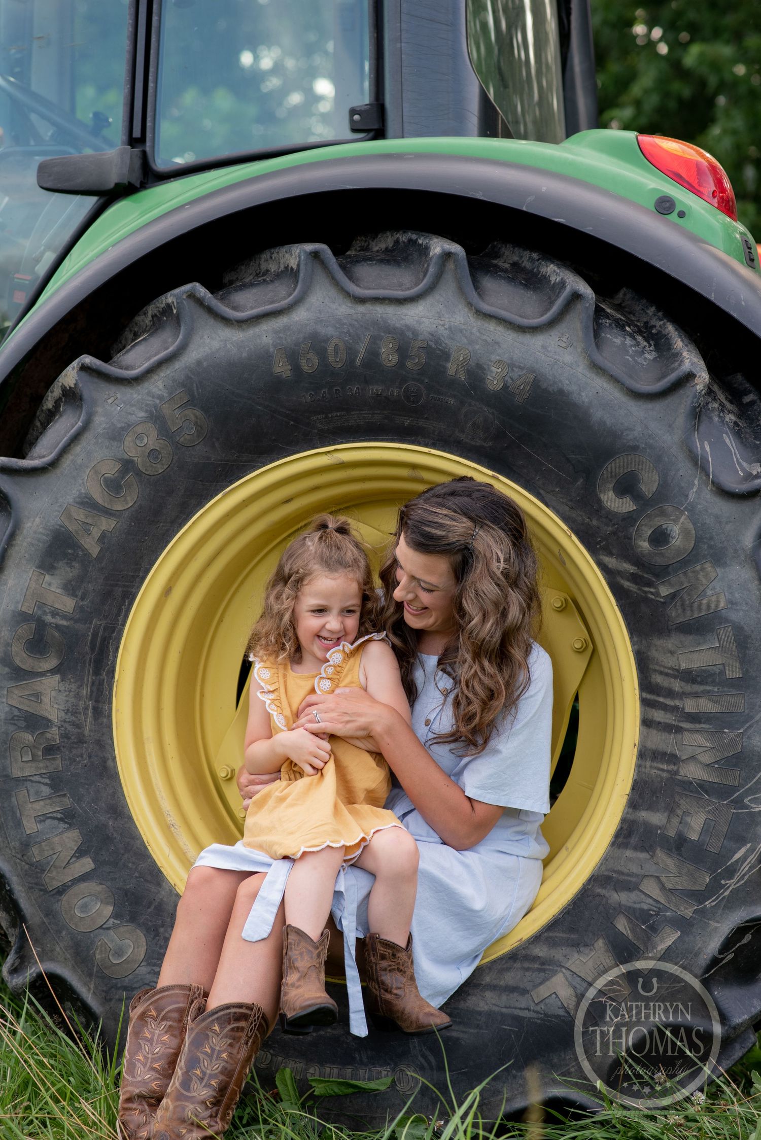 Two people share a sweet moment while sitting inside a large tractor wheel on a farm.