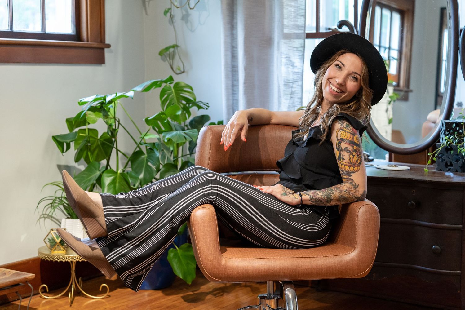 A relaxed woman reclines on a brown leather chair in a bright room with indoor plants.