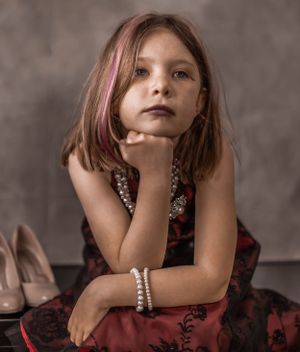 Studio portrait featuring someone in a red dress with pearl bracelets against a gray background.