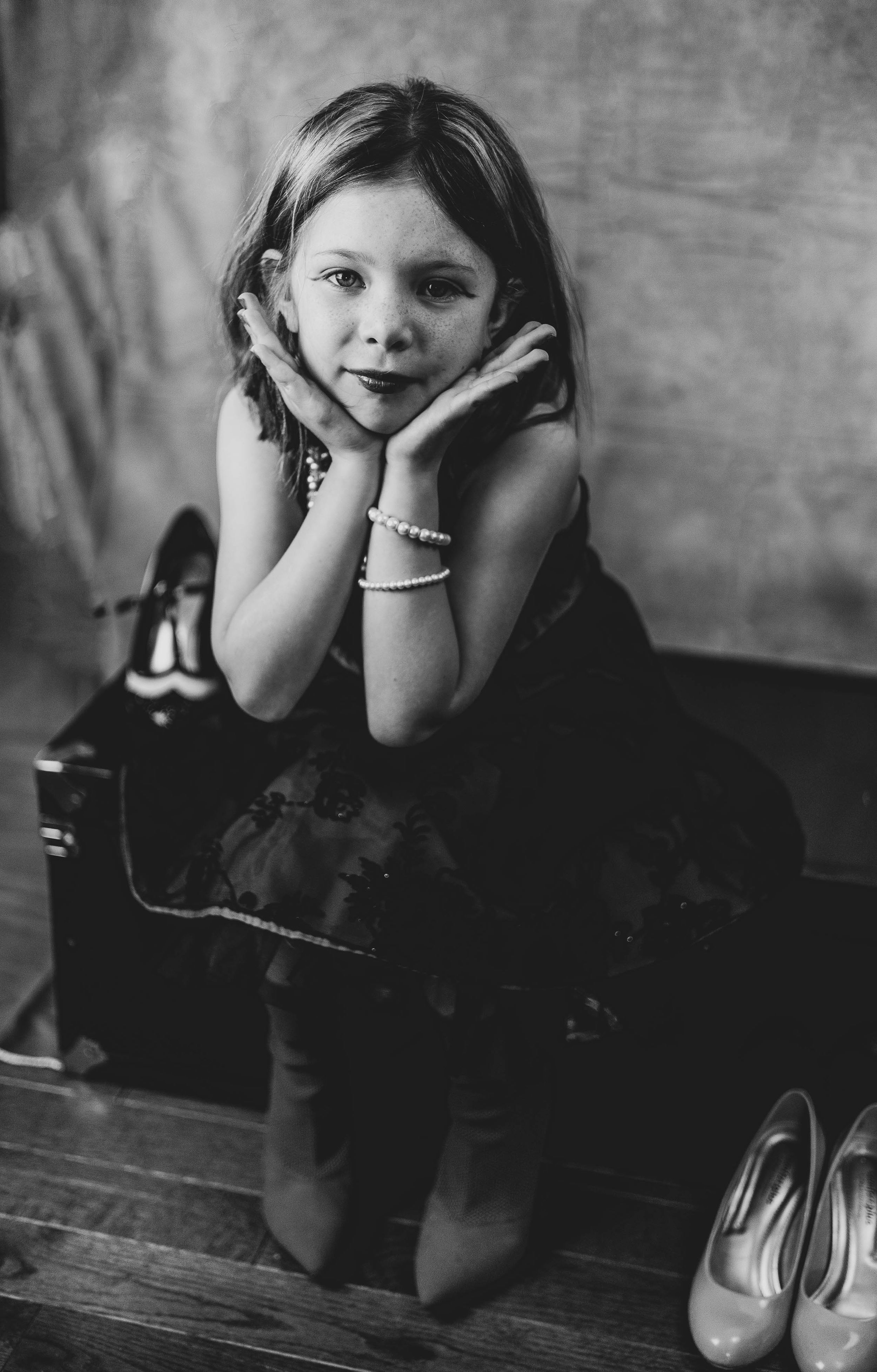 Black and white portrait of someone posing on a trunk with hands framing their face.