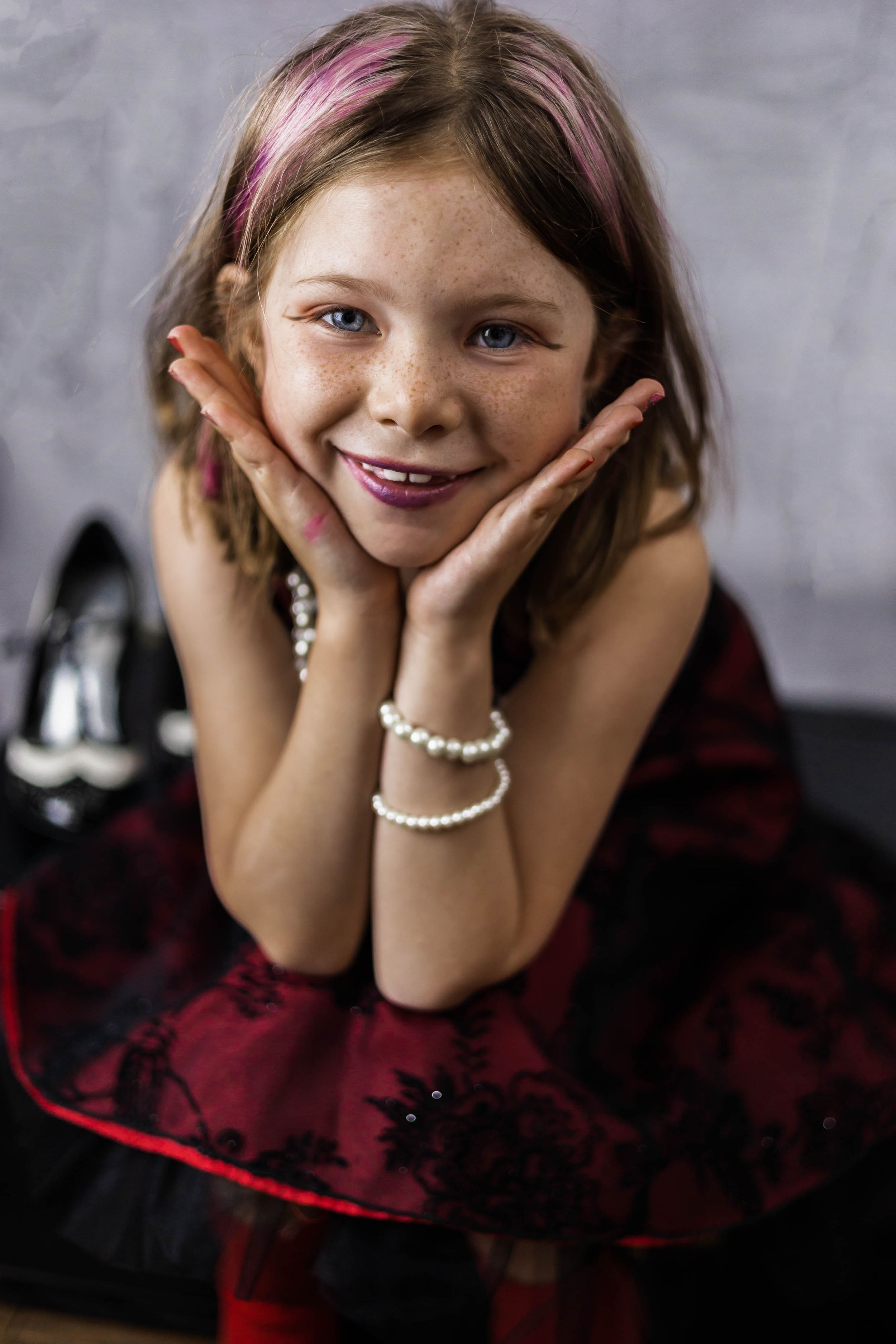 Young performer in a red dress poses playfully with hands framing face.