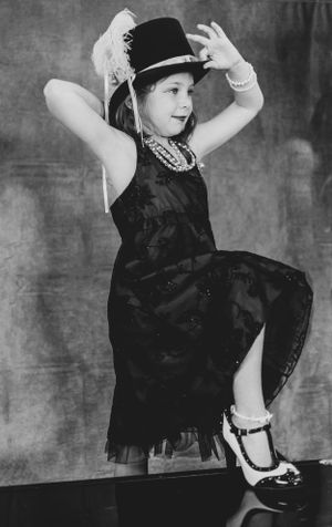 Theatrical dance poses on piano in black dress and top hat.