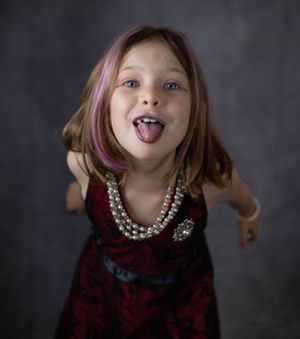 Playful upward angles capture someone in a burgundy dress with pearl necklace against dark background.