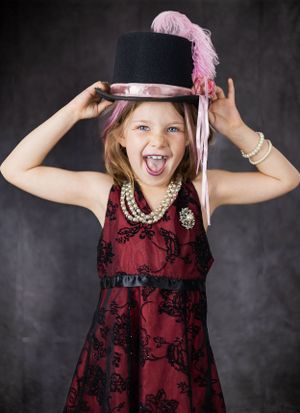 Energetic poses with a pink feathered top hat and burgundy dress against gray background.