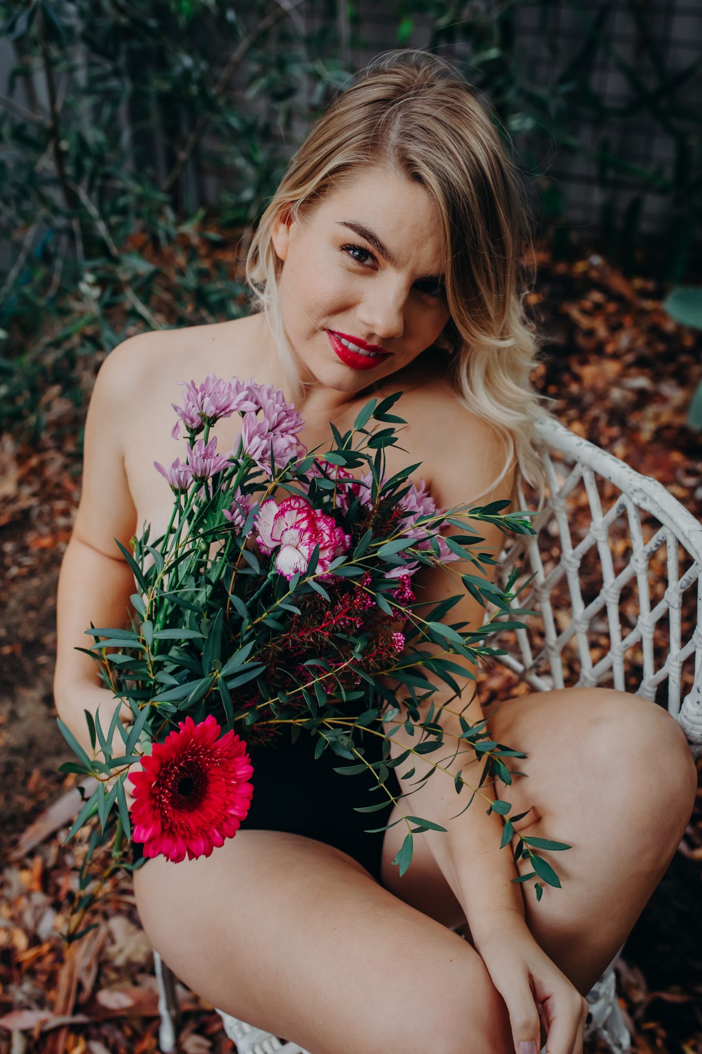 Woman in black swimsuit poses with vibrant bouquet featuring red gerbera daisy and purple flowers.