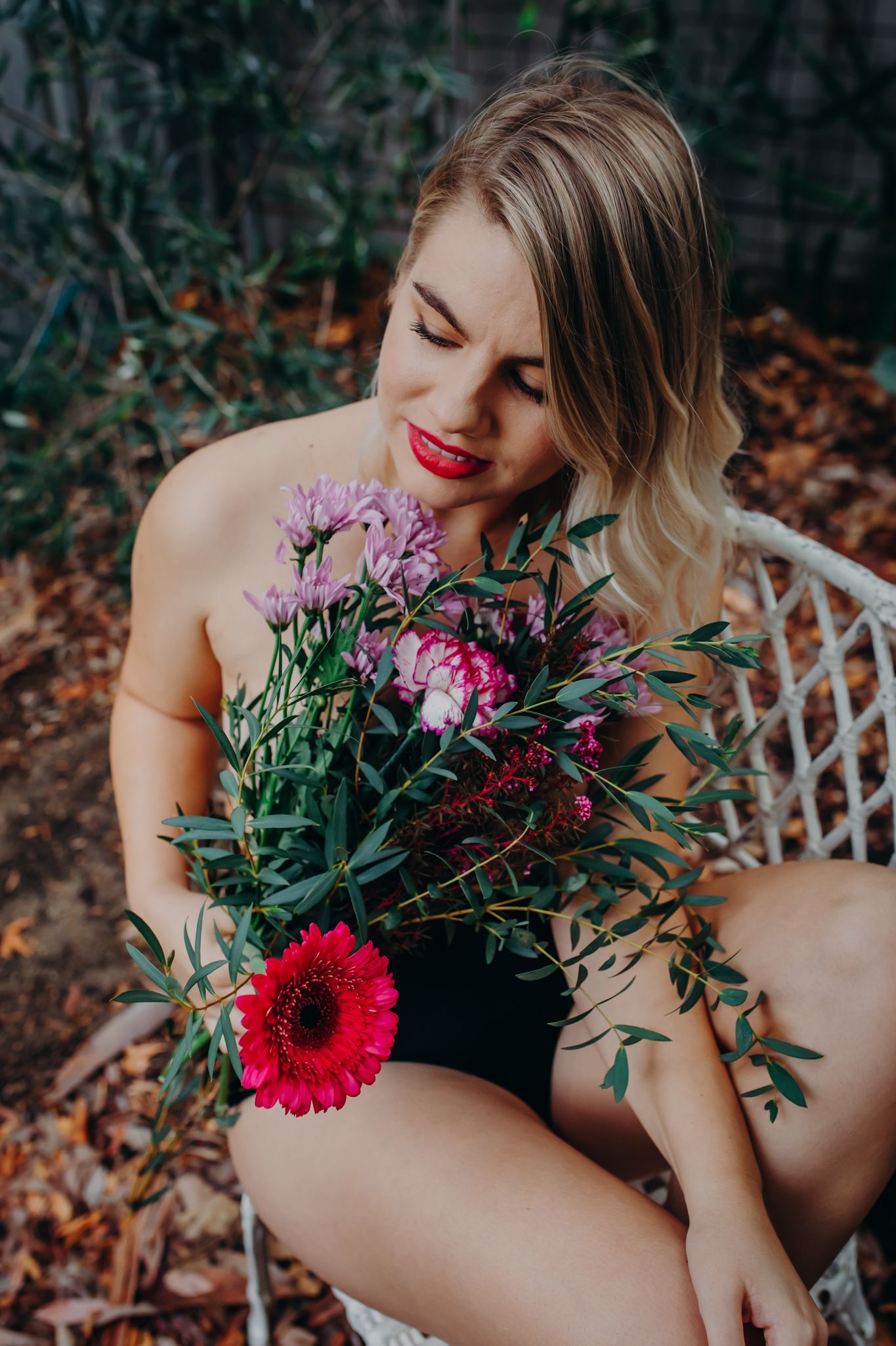 Artistic portrait with floral arrangement featuring pink and red blooms against outdoor garden setting.