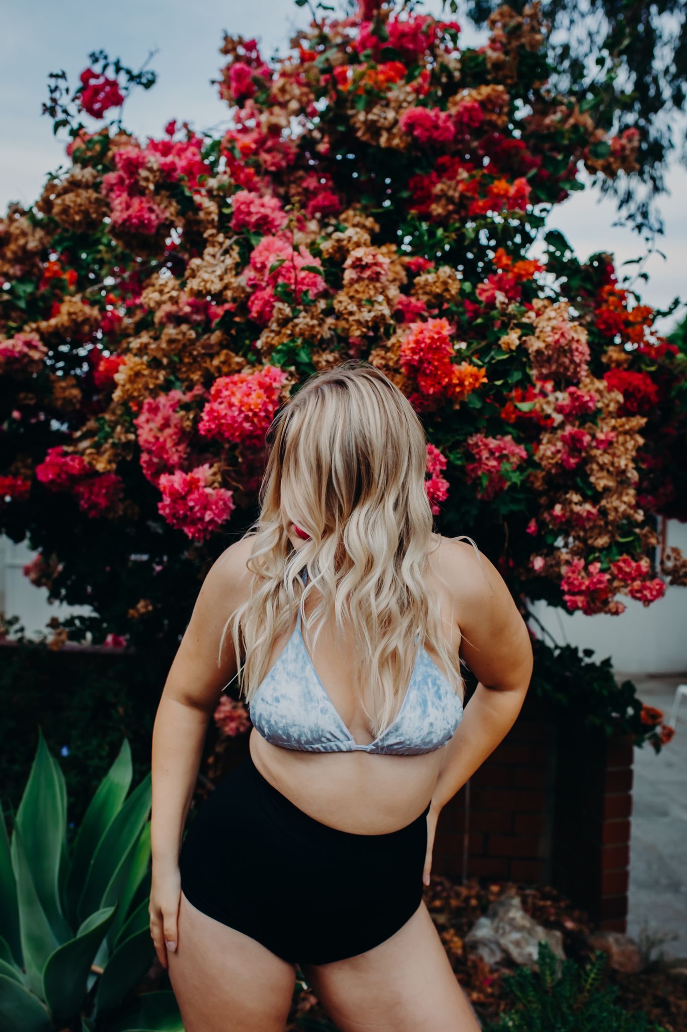 Modern swimwear shoot featuring silver bikini top against blooming bougainvillea bush.