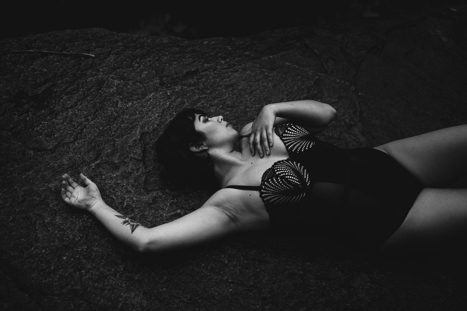 Dramatic black and white boudoir photo of a model lying on dark ground.