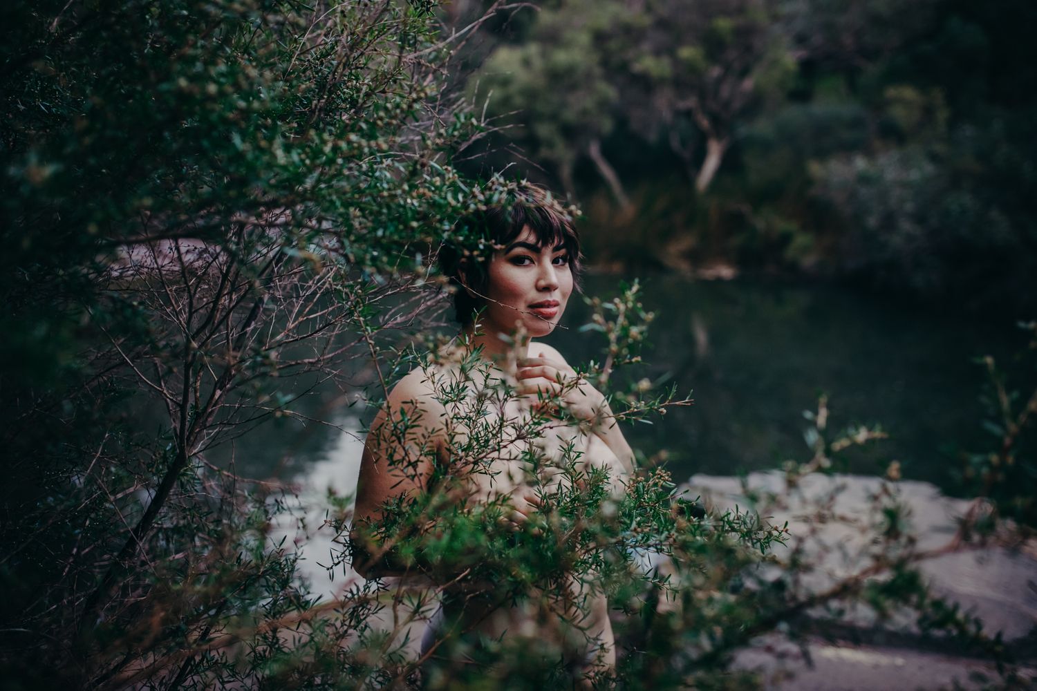 Artistic outdoor portrait with foliage framing against dark moody water.