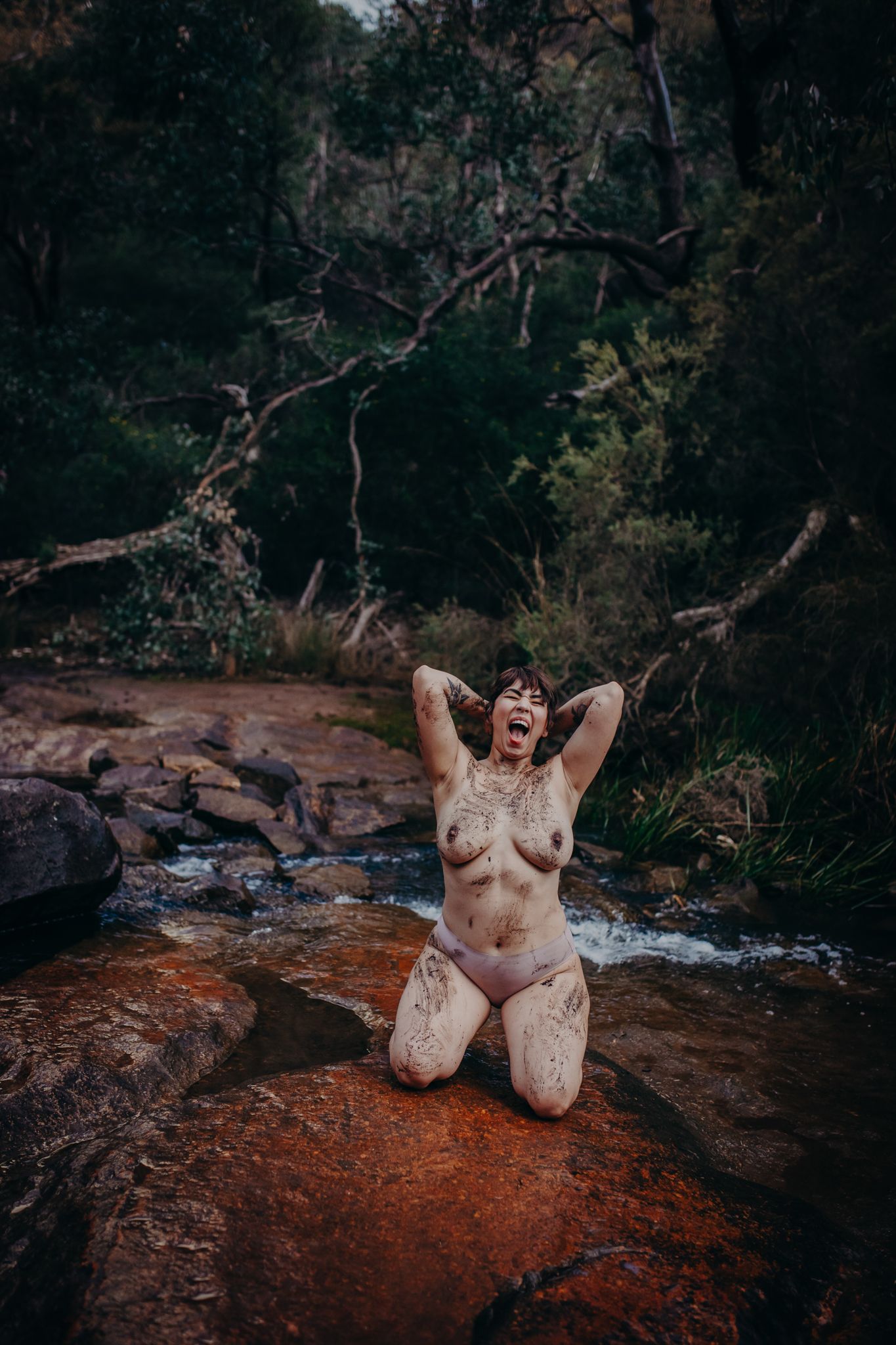 Expressive outdoor portrait on rust-colored rocks in a secluded forest setting.