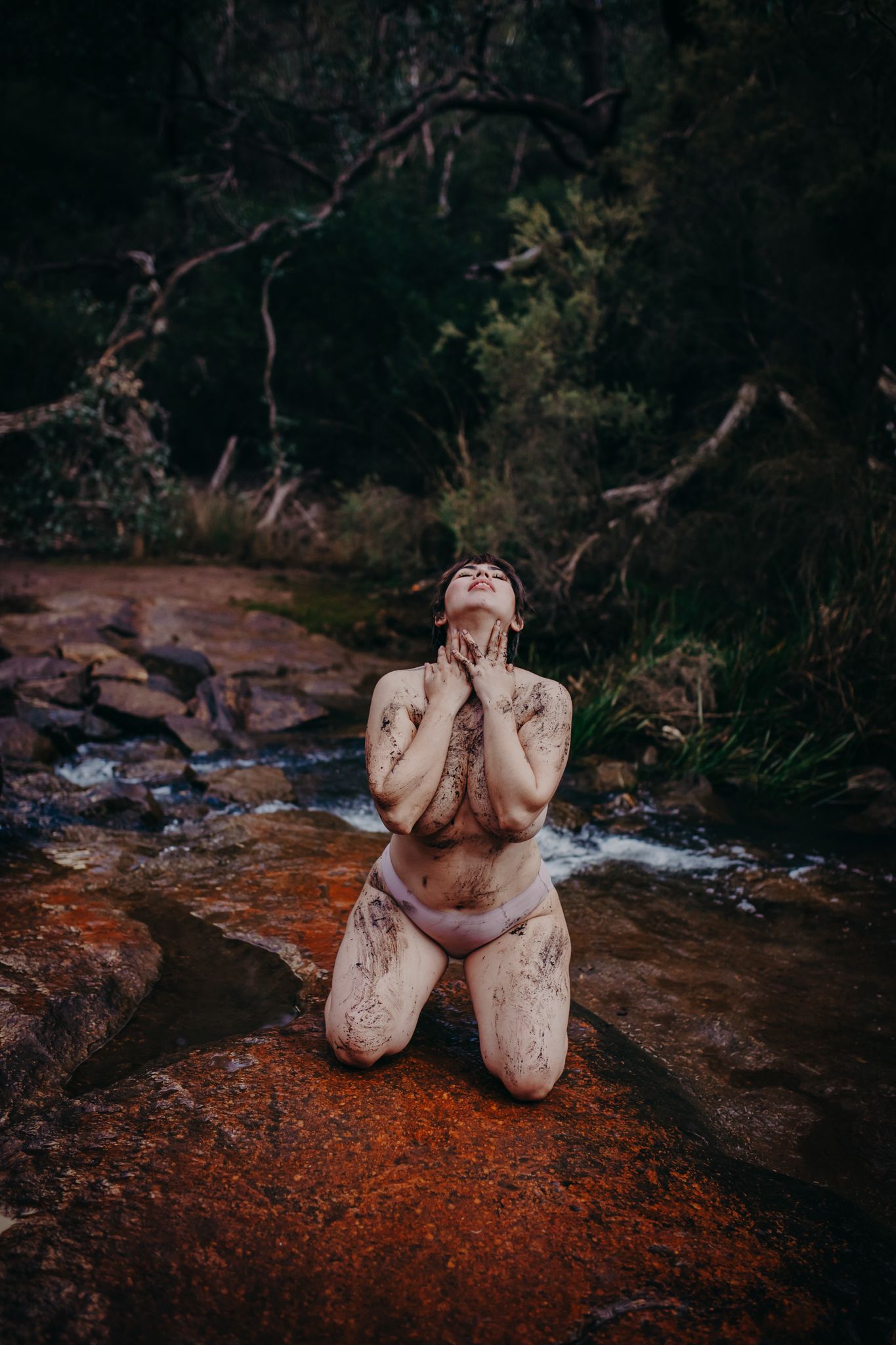 Emotive artistic portrait captured on natural rock formations in dappled forest light.
