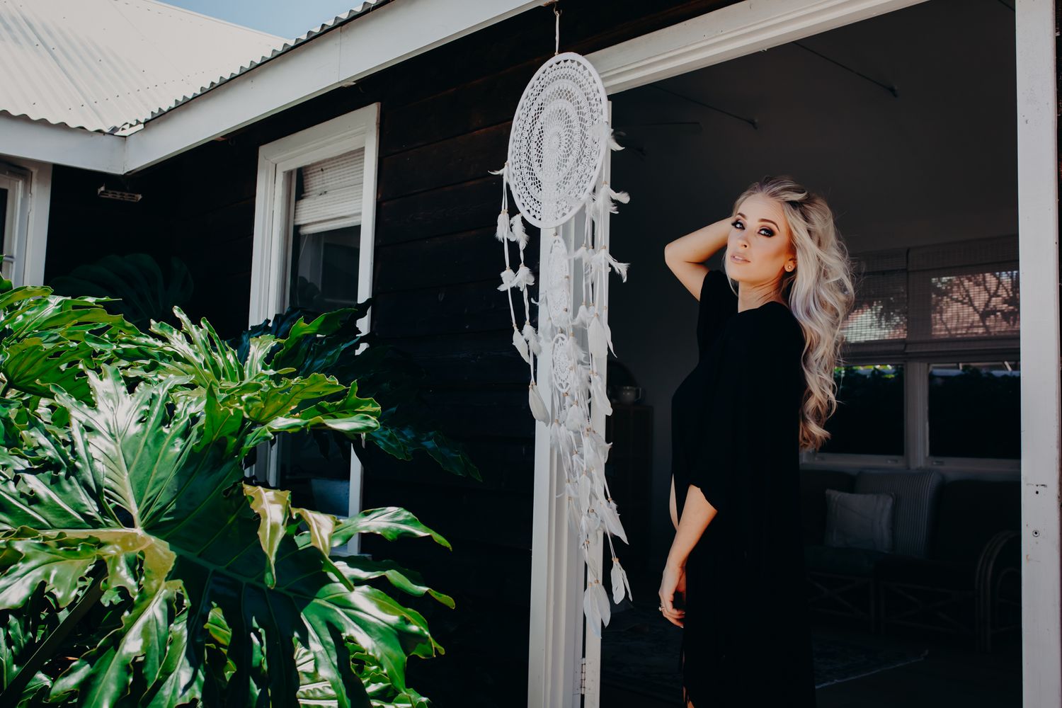 Outdoor portrait with dreamcatcher and tropical plants against black building.