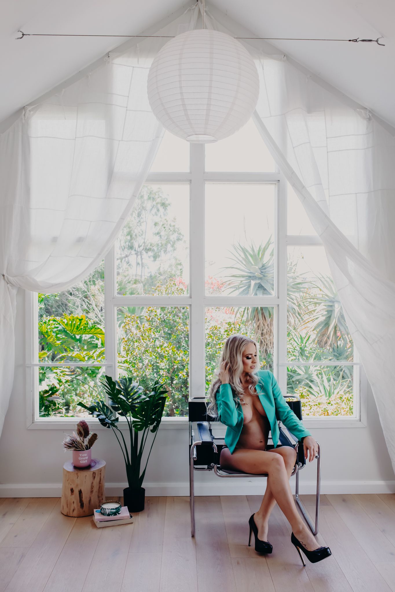 Stylish portrait in sunlit room with white curtains and tropical plants.