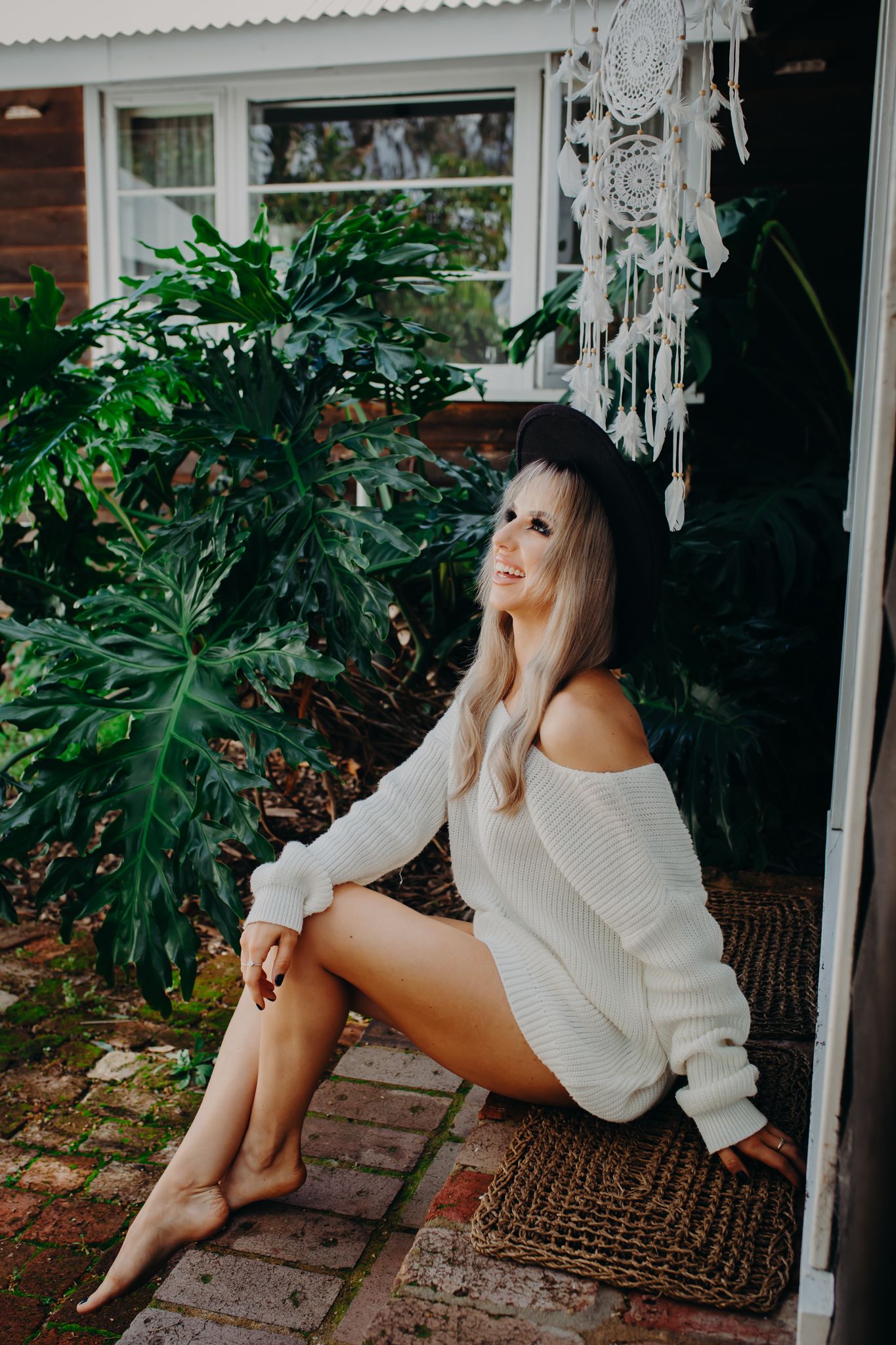 Casual portrait by house entrance with hanging macrame and lush garden backdrop.