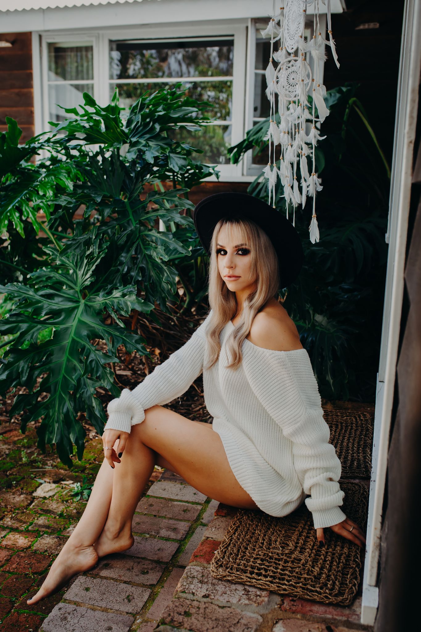 Artistic portrait with black hat and oversized sweater against white window frame.