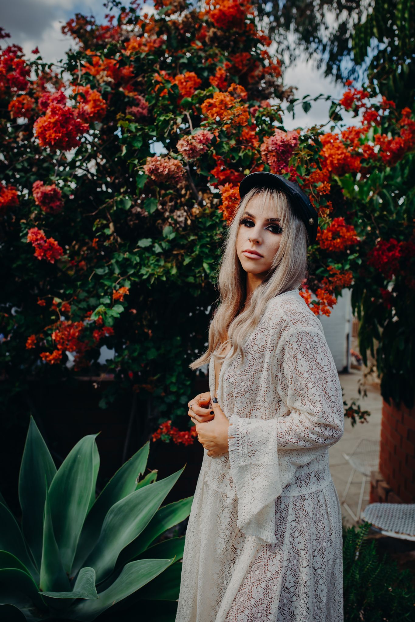 Romantic portrait in white lace dress among vibrant red flowering bushes.