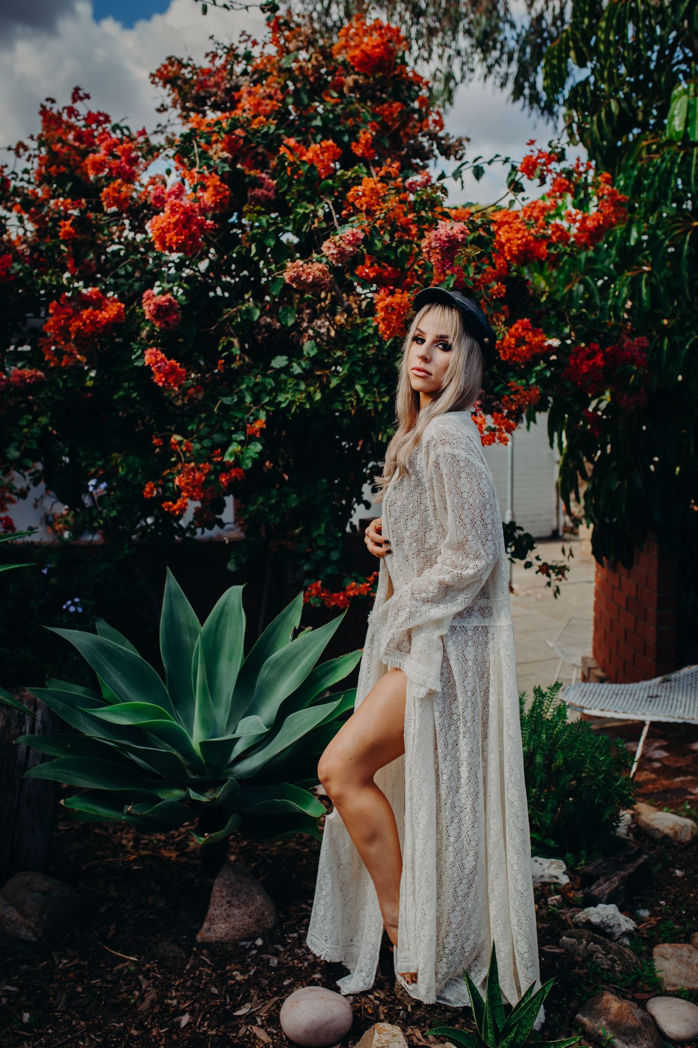 Lace gown photoshoot in garden with blooming orange flowers and large agave plant.