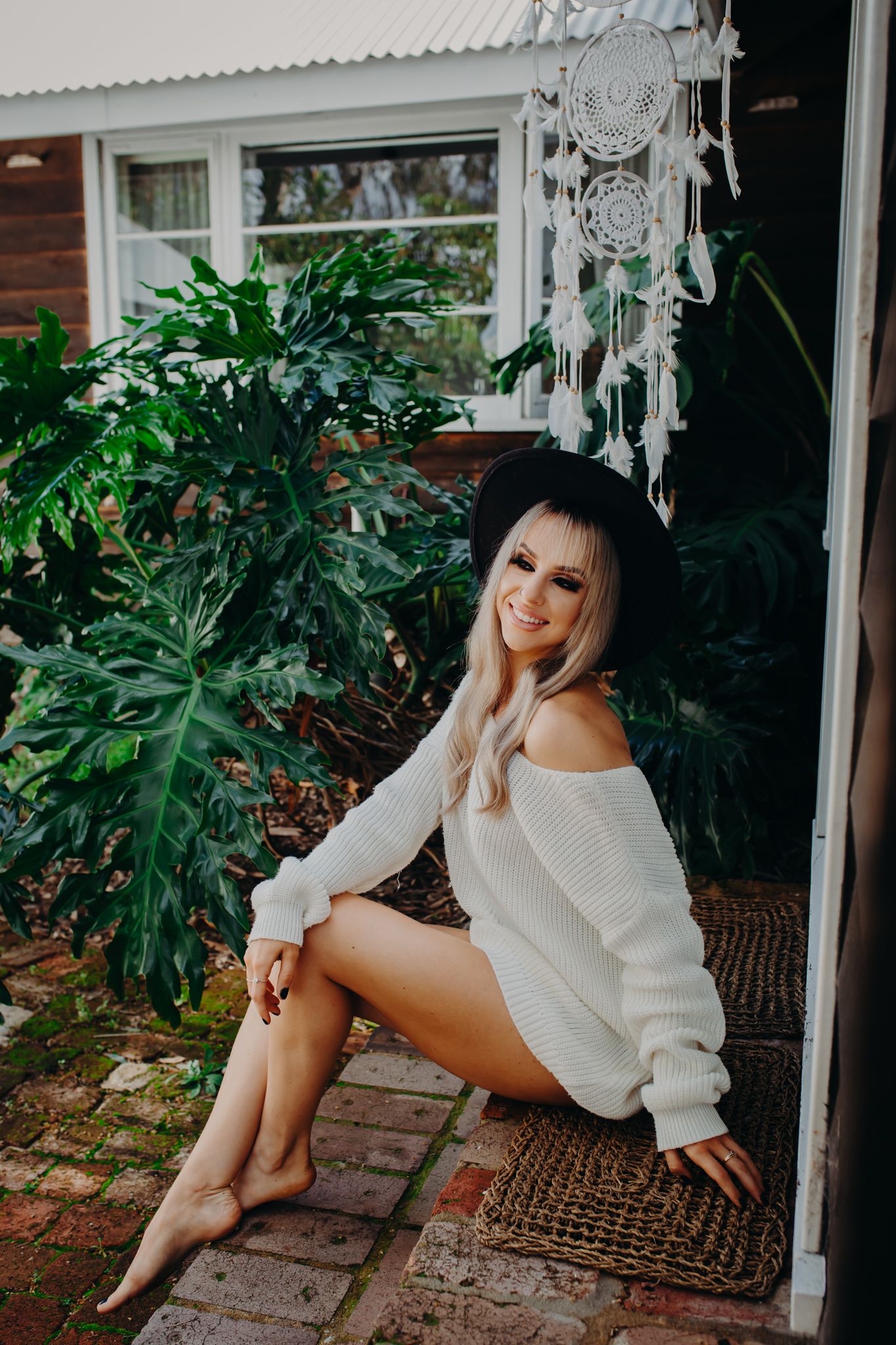 Cozy winter sweater photoshoot on brick patio with dreamcatcher and tropical plants.
