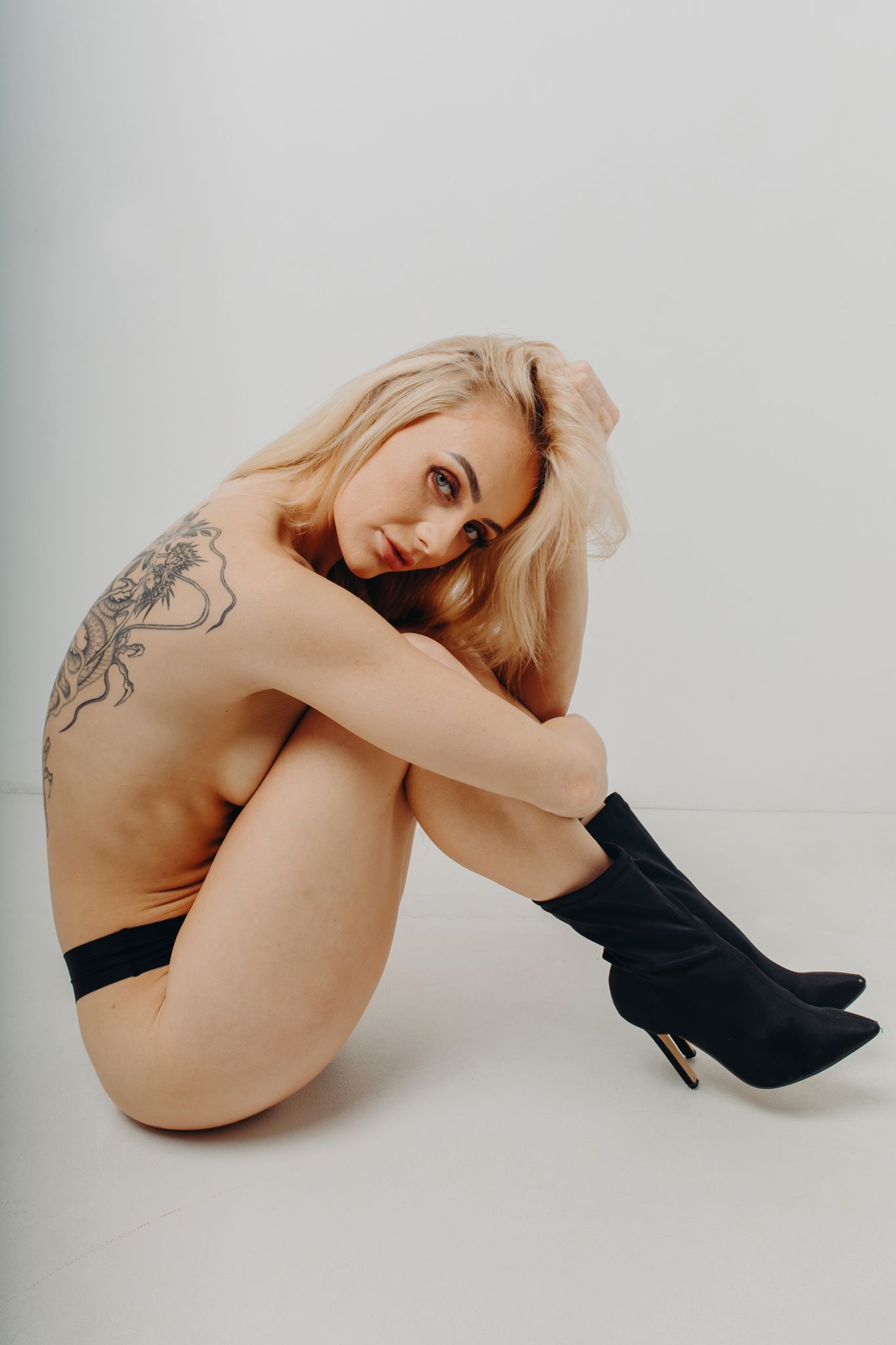 Artistic nude portrait with black boots showing intricate shoulder tattoo.