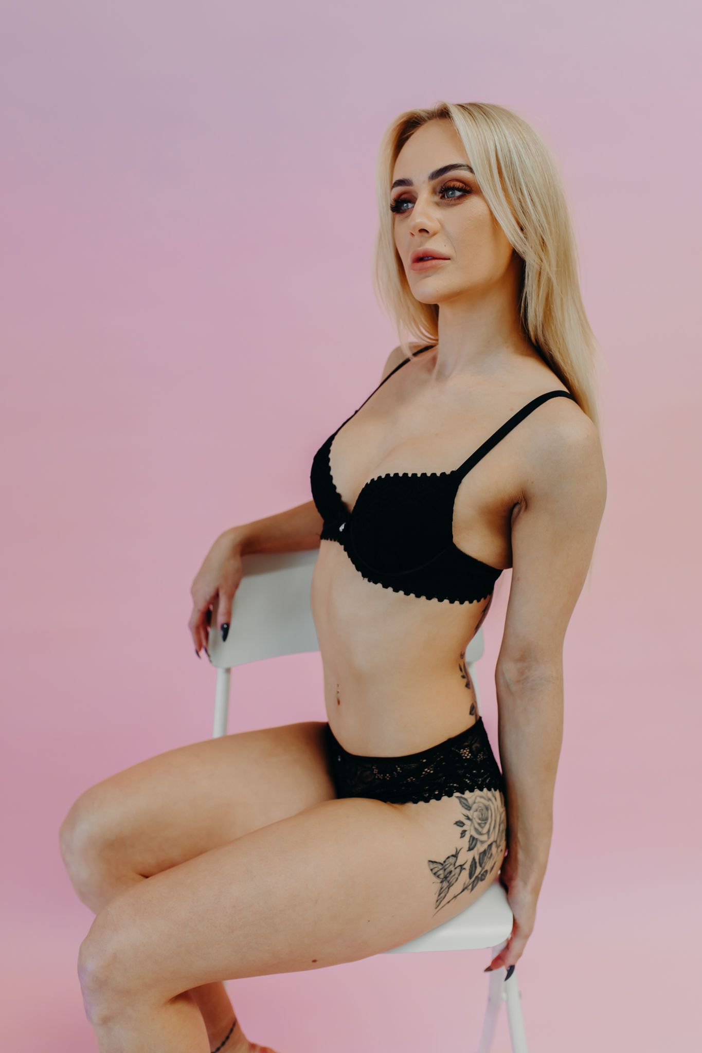 Artistic lingerie photo with black lace set against pink background shows model with tattoo on hip.