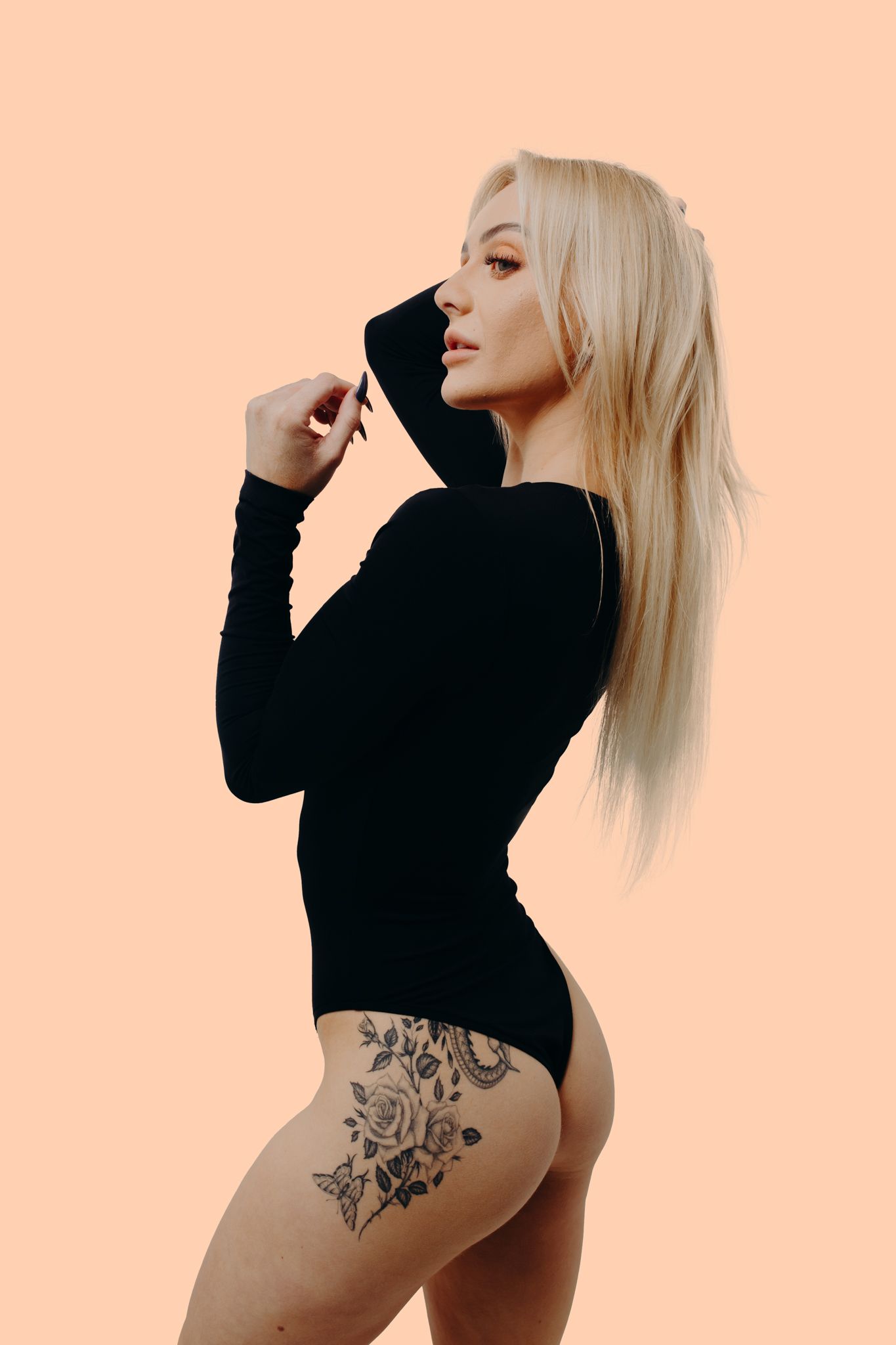 Side profile pose in fitted black bodysuit highlighting floral tattoo artwork.