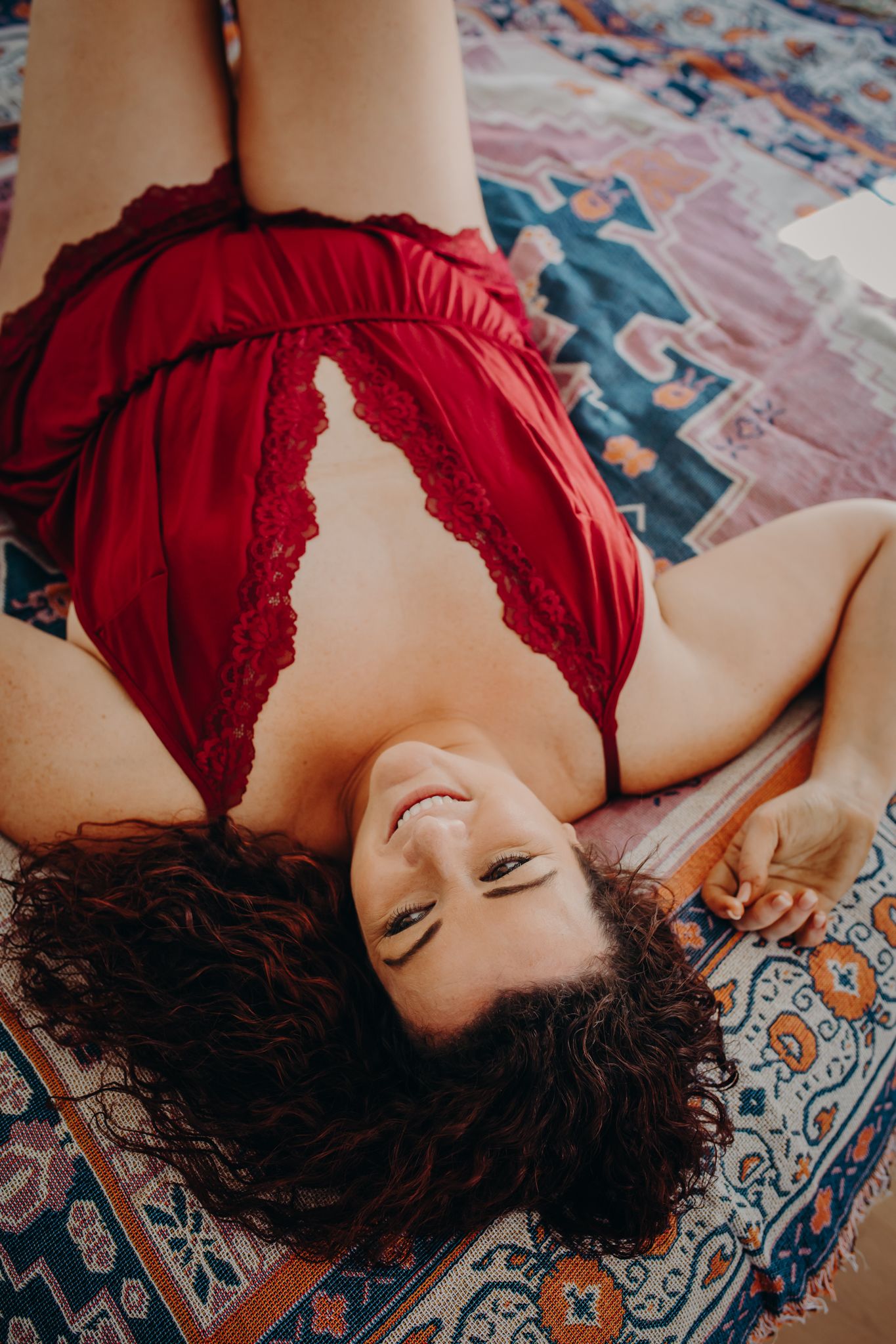 Intimate boudoir portrait on patterned rug in red lace lingerie.