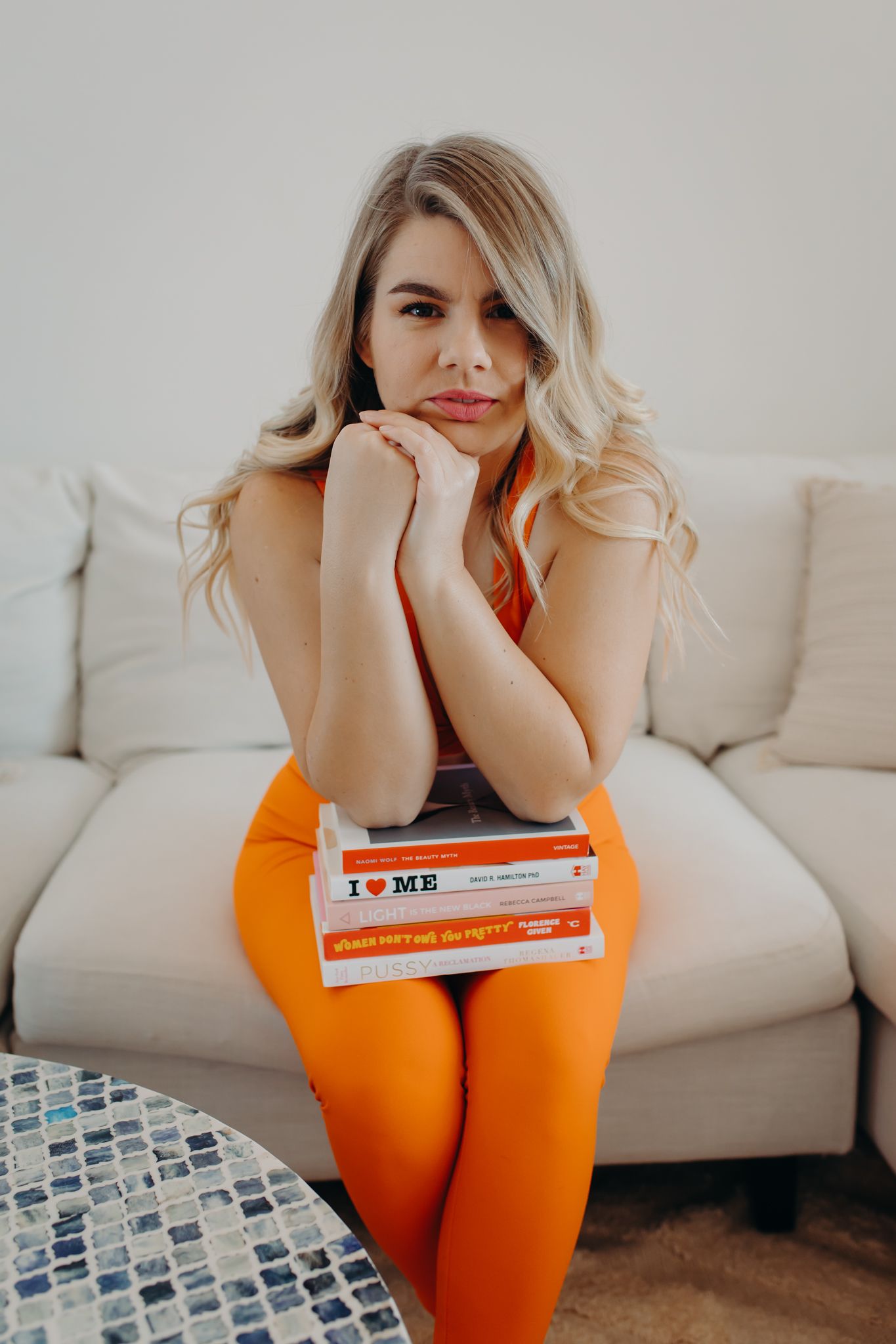 Lifestyle photo of someone in bright orange leggings sitting casually on beige couch.