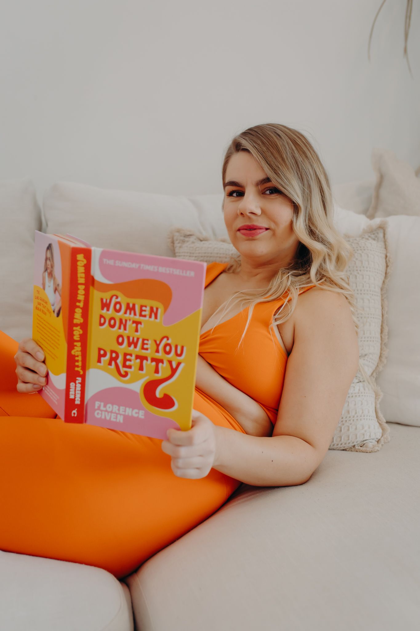 Reader relaxing on couch in orange activewear while reading self-help book.