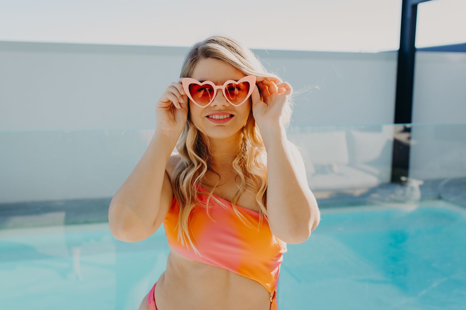 Summer poolside portrait with red heart-shaped sunglasses and orange swimwear.