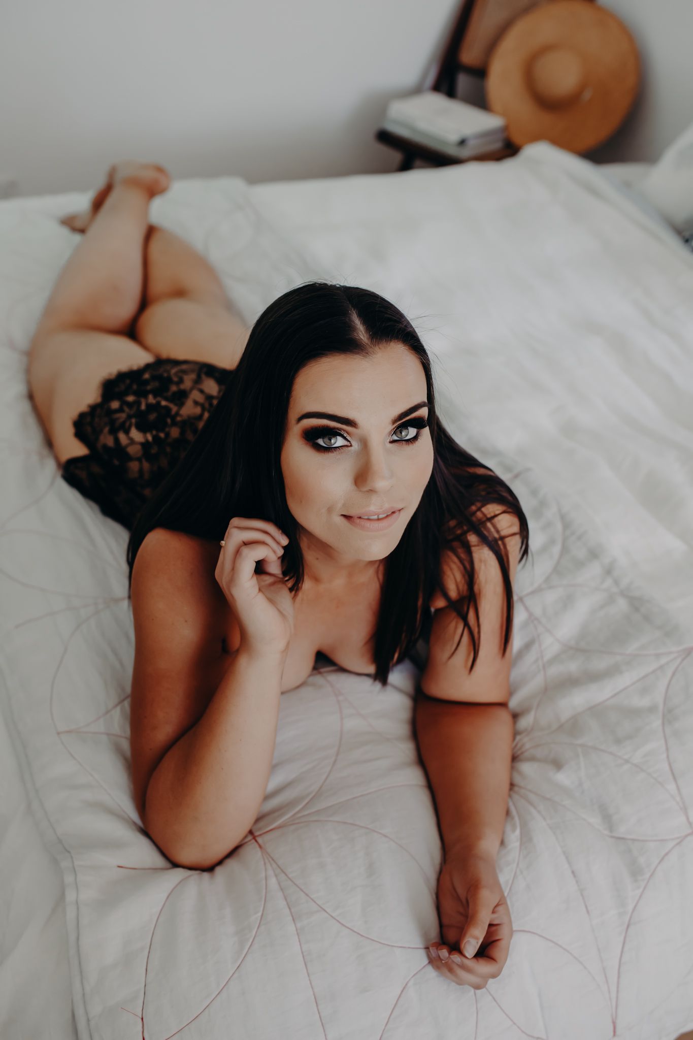 Intimate bedroom portrait with black lace details on white bedding.