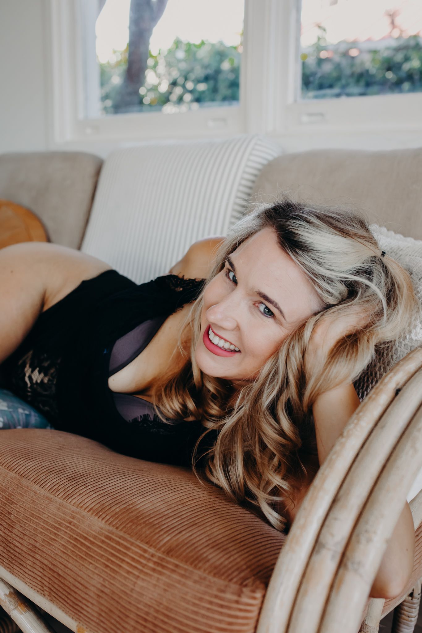 Person in black lying on brown corduroy couch smiling at camera.