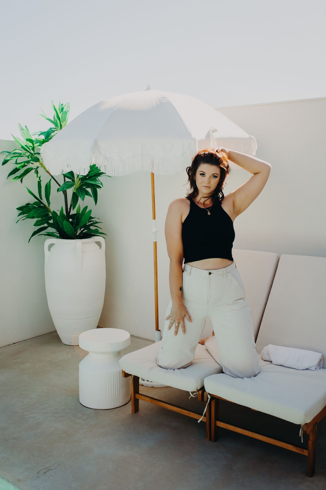 Person in black crop top and white pants posing on a modern outdoor lounge with decorative plants.