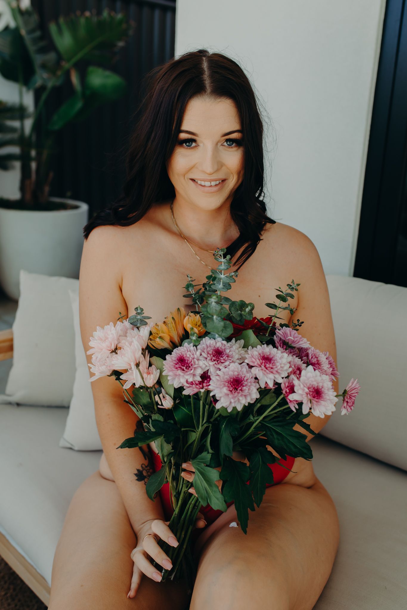 Person holding vibrant pink and yellow flower bouquet while sitting on white outdoor furniture.